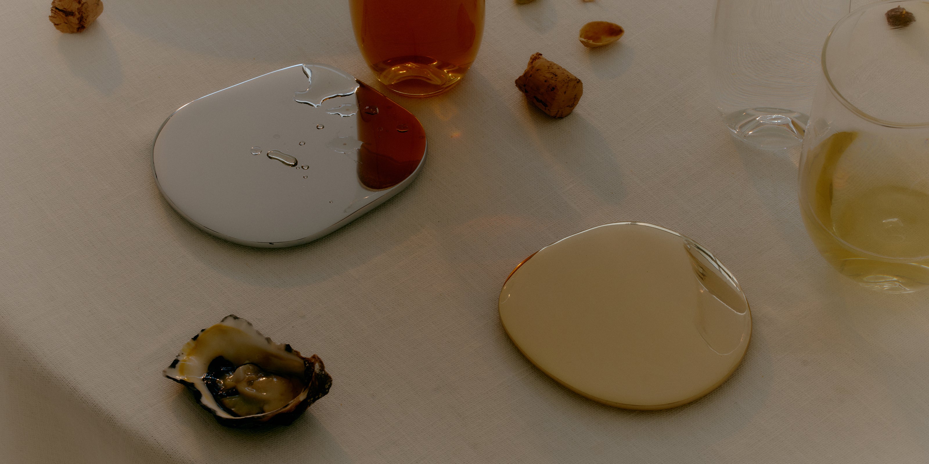 Brass and silver cocktail coasters by designer Corey Ashford styled on a summer table with oysters, wine and natural light.