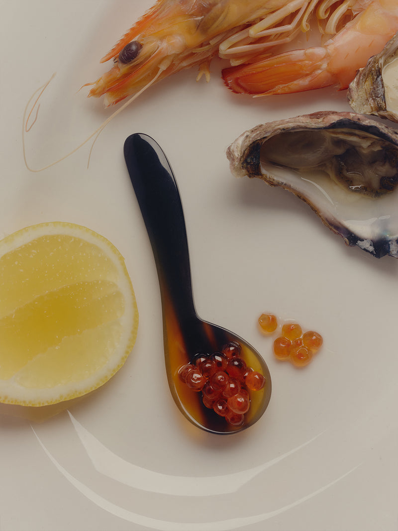 COREY ASHFORD hand-sculpted horn caviar spoon in amber tortoise finish. Features scoop of salmon roe alongside oysters, prawns and juicy lemon.