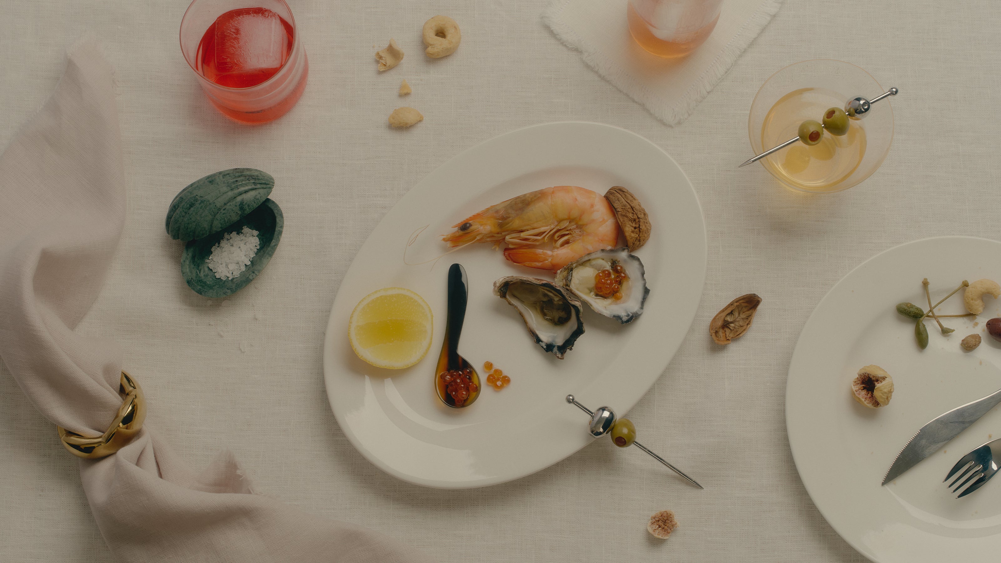 COREY ASHFORD L’Apéritif Holiday Collection - oyster, caviar spoon, martini with olive cocktail pick, marble salt dish and napkin ring styled on a linen table.